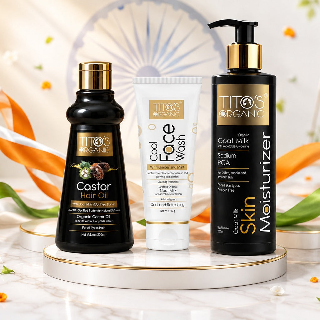 Three Titos Organics skincare products displayed on a white marble surface with festive Indian decorations: a black Castor Hair Oil bottle, a white Cool Face Wash tube, and a black Skin Moisturizer pump bottle, surrounded by orange marigold flowers and orange-and-green ribbon.